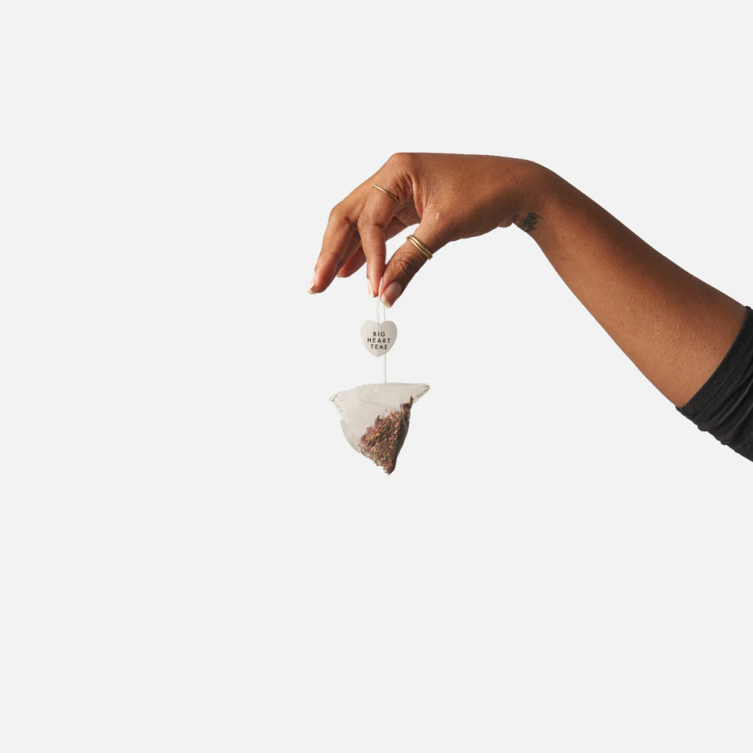 Heart-shaped tea sachet held by hand with a small circular label